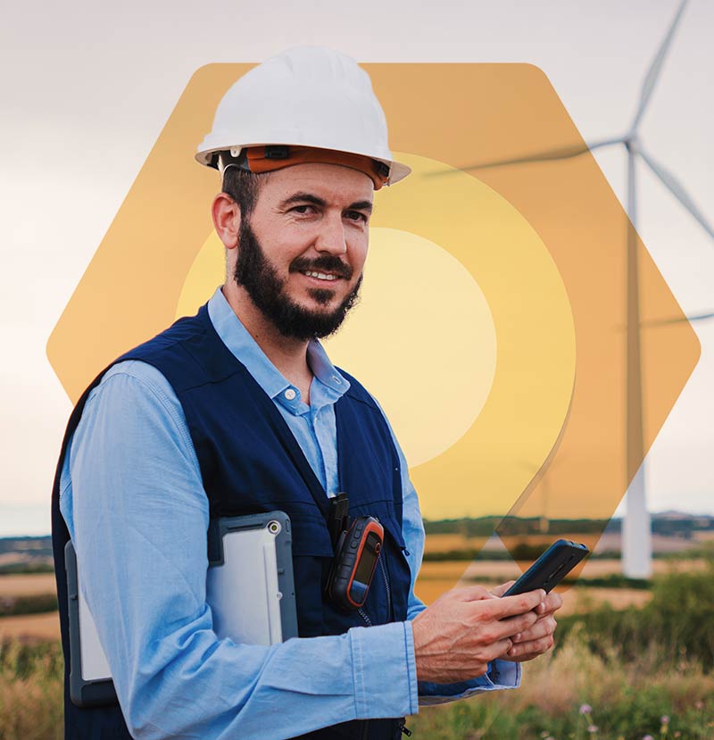 dynamics-365-field-service-techniker Das Bild zeigt einen Mitarbeiter mit Baustellenhelm vor Windrädern. Er nutzt Dynamics 365 Field Service auf dem Smartphone.